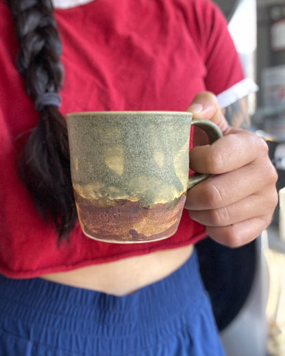 Handthrown ceramic mug, sage matte glazed with amber-iron oxide wash. Dual-texture surface, matte. Rock-hammered hand-textured rugged mountain landscape, hand-pulled handle.