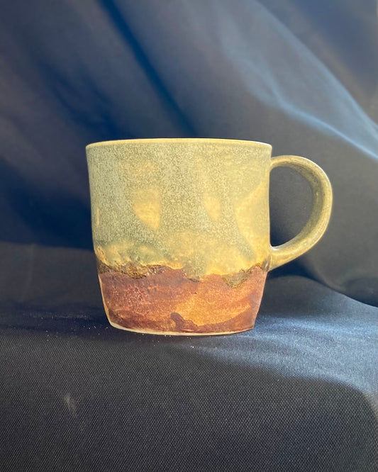 Handthrown ceramic mug, sage matte glazed with amber-iron oxide wash. Dual-texture surface, matte. Rock-hammered hand-textured rugged mountain landscape, hand-pulled handle.