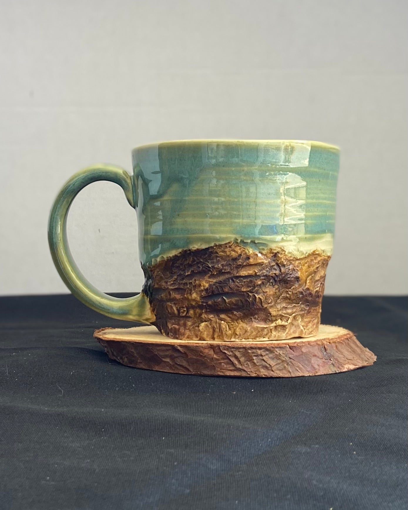 Handcrafted Mountain Mug with glossy celadon sky glaze and rocky textured mountainscape, accented with iron oxide and matte amber quartz glaze. Unique ceramic mug inspired by outdoor rock climbing, perfect for coffee or tea. Artisan quality, wabi sabi design, and playful glaze details