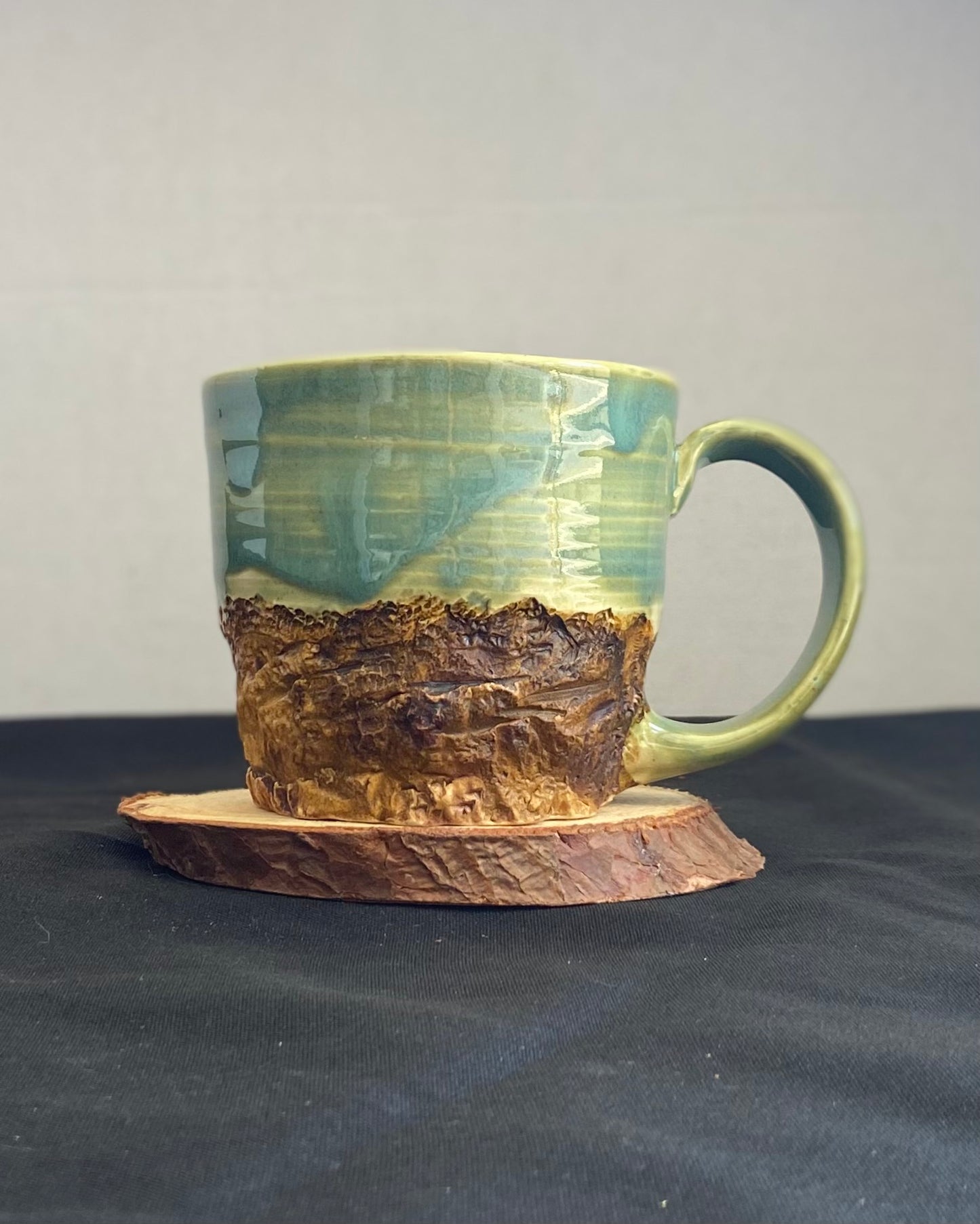 Handcrafted Mountain Mug with glossy celadon sky glaze and rocky textured mountainscape, accented with iron oxide and matte amber quartz glaze. Unique ceramic mug inspired by outdoor rock climbing, perfect for coffee or tea. Artisan quality, wabi sabi design, and playful glaze details