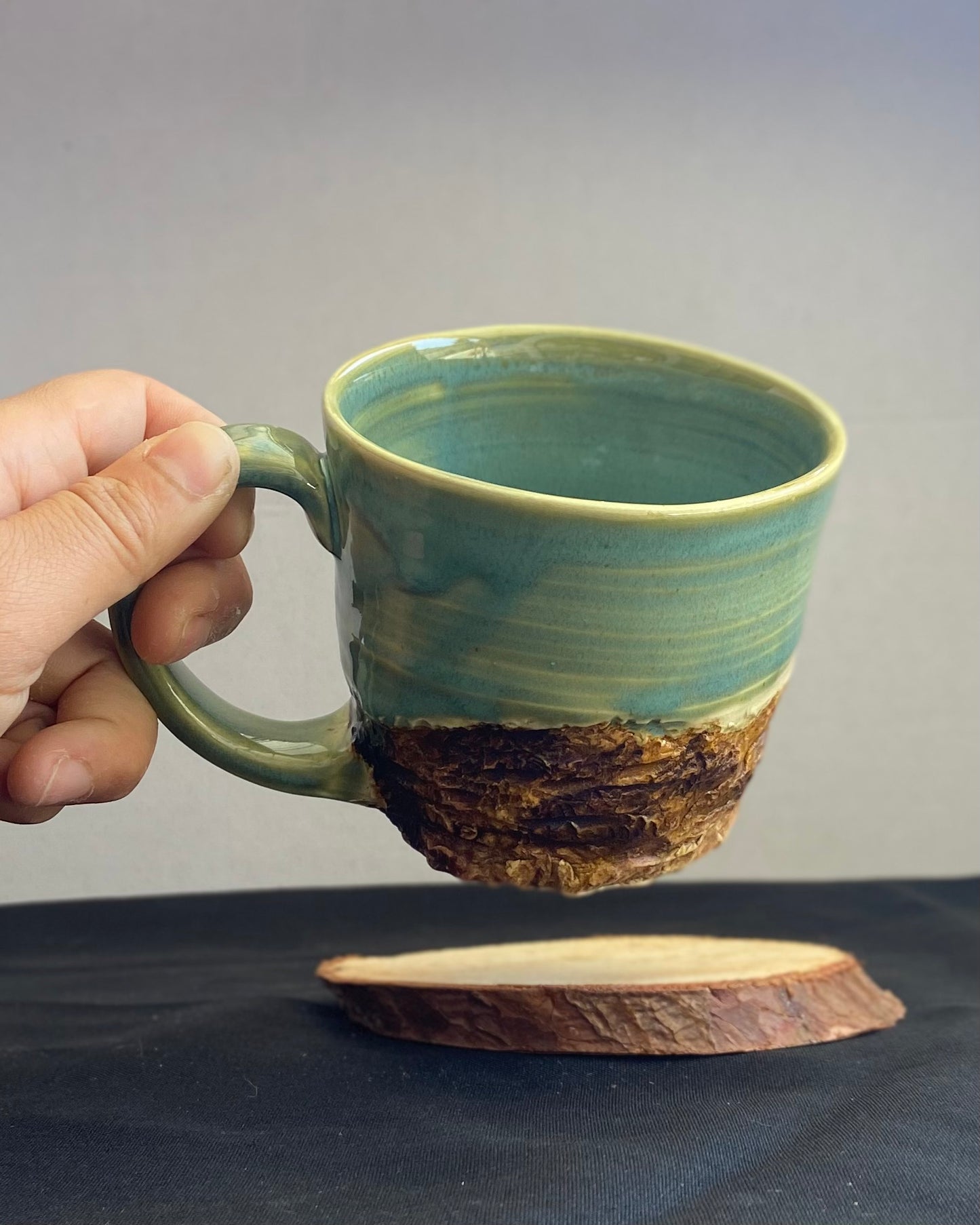 Handcrafted Mountain Mug with glossy celadon sky glaze and rocky textured mountainscape, accented with iron oxide and matte amber quartz glaze. Unique ceramic mug inspired by outdoor rock climbing, perfect for coffee or tea. Artisan quality, wabi sabi design, and playful glaze details