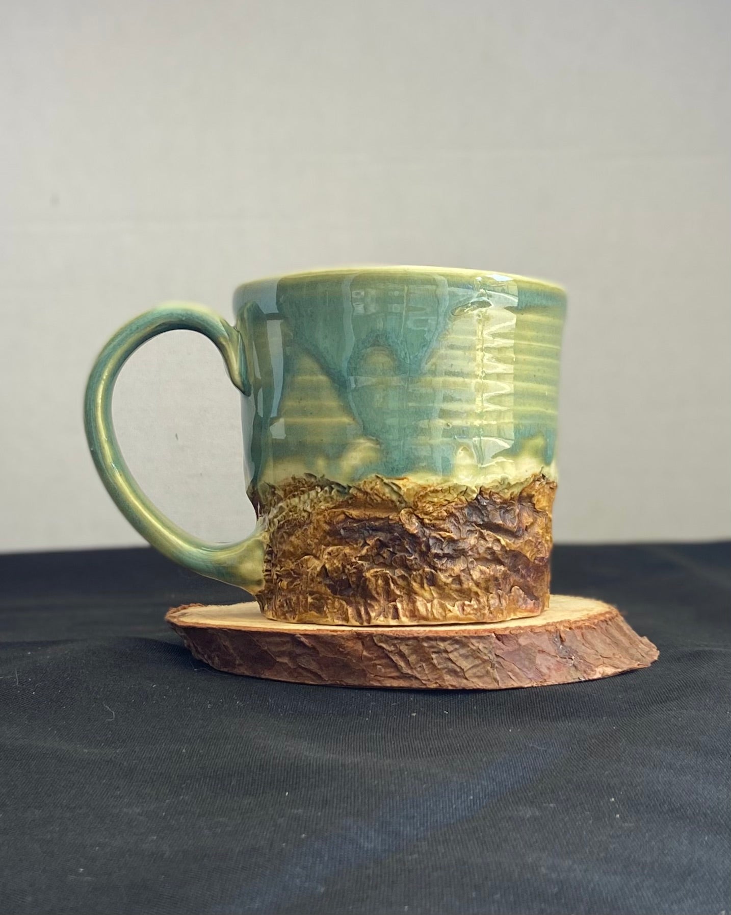 Handcrafted Mountain Mug with glossy celadon sky glaze and rocky textured mountainscape, accented with iron oxide and matte amber quartz glaze. Unique ceramic mug inspired by outdoor rock climbing, perfect for coffee or tea. Artisan quality, wabi sabi design, and playful glaze details