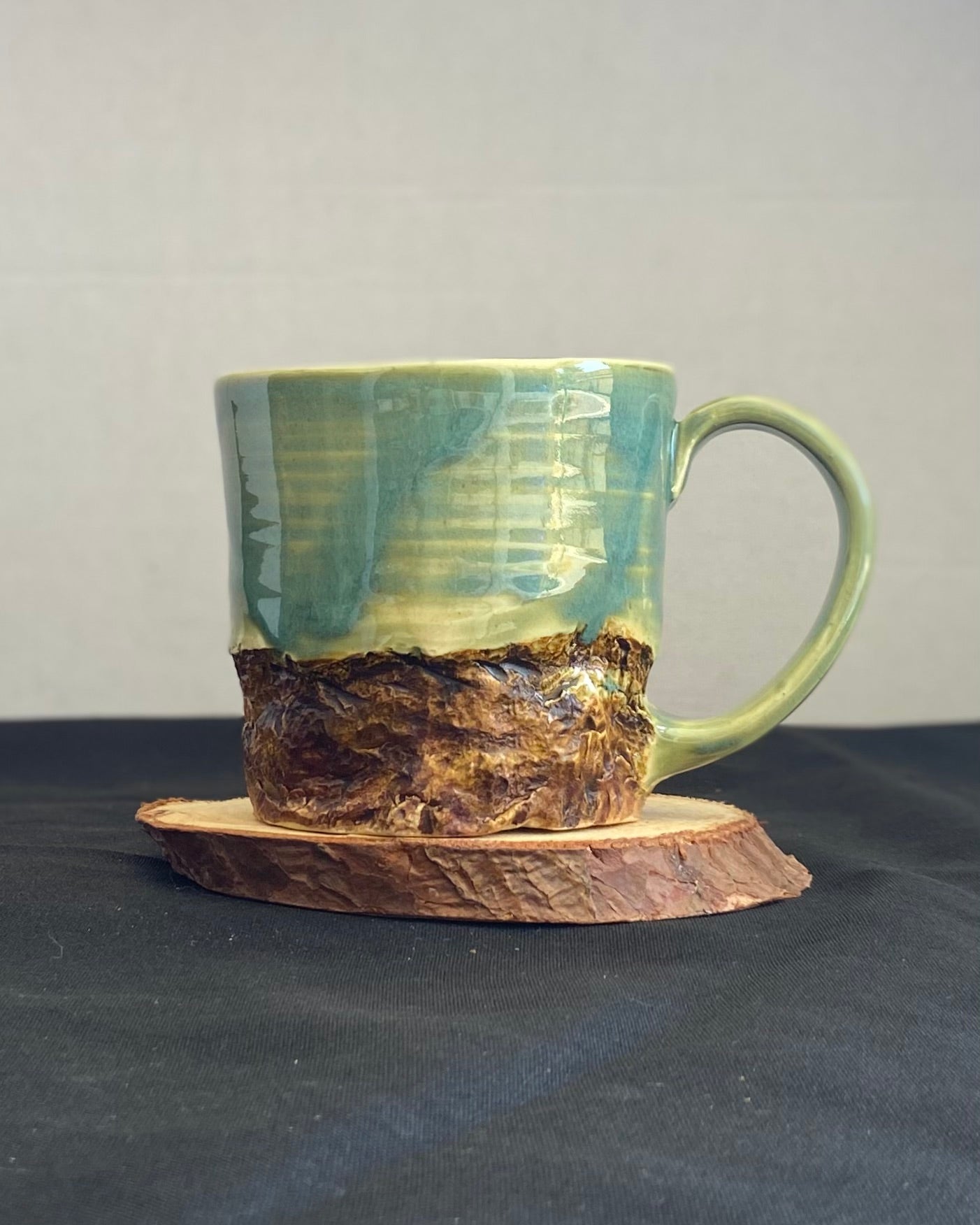 Handcrafted Mountain Mug with glossy celadon sky glaze and rocky textured mountainscape, accented with iron oxide and matte amber quartz glaze. Unique ceramic mug inspired by outdoor rock climbing, perfect for coffee or tea. Artisan quality, wabi sabi design, and playful glaze details