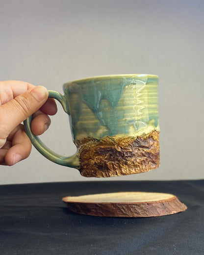 Handcrafted Mountain Mug with glossy celadon sky glaze and rocky textured mountainscape, accented with iron oxide and matte amber quartz glaze. Unique ceramic mug inspired by outdoor rock climbing, perfect for coffee or tea. Artisan quality, wabi sabi design, and playful glaze details