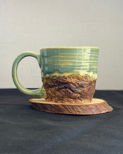 Handcrafted Mountain Mug with glossy celadon sky glaze and rocky textured mountainscape, accented with iron oxide and matte amber quartz glaze. Unique ceramic mug inspired by outdoor rock climbing, perfect for coffee or tea. Artisan quality, wabi sabi design, and playful glaze details