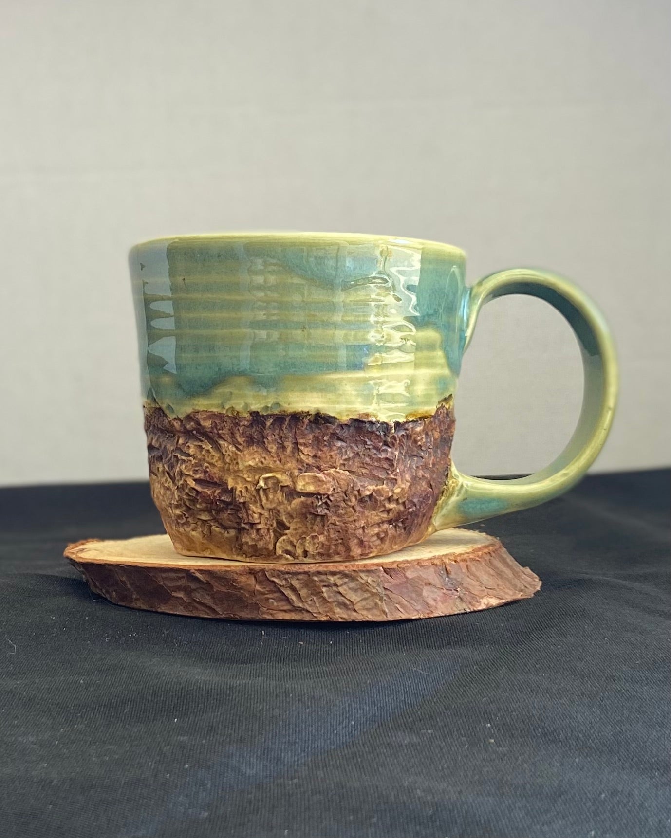 Handcrafted Mountain Mug with glossy celadon sky glaze and rocky textured mountainscape, accented with iron oxide and matte amber quartz glaze. Unique ceramic mug inspired by outdoor rock climbing, perfect for coffee or tea. Artisan quality, wabi sabi design, and playful glaze details