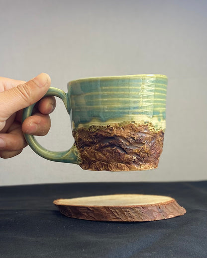 Handcrafted Mountain Mug with glossy celadon sky glaze and rocky textured mountainscape, accented with iron oxide and matte amber quartz glaze. Unique ceramic mug inspired by outdoor rock climbing, perfect for coffee or tea. Artisan quality, wabi sabi design, and playful glaze details