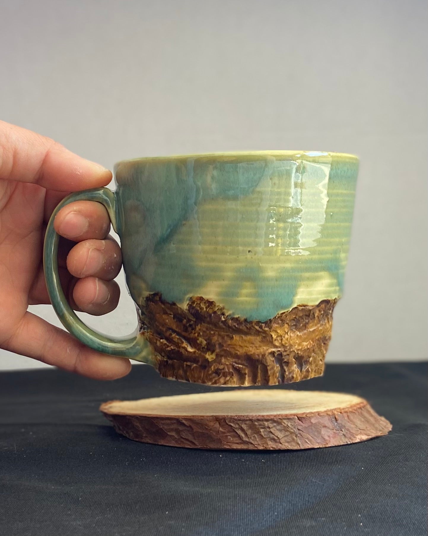 Handcrafted Mountain Mug with glossy celadon sky glaze and rocky textured mountainscape, accented with iron oxide and matte amber quartz glaze. Unique ceramic mug inspired by outdoor rock climbing, perfect for coffee or tea. Artisan quality, wabi sabi design, and playful glaze details