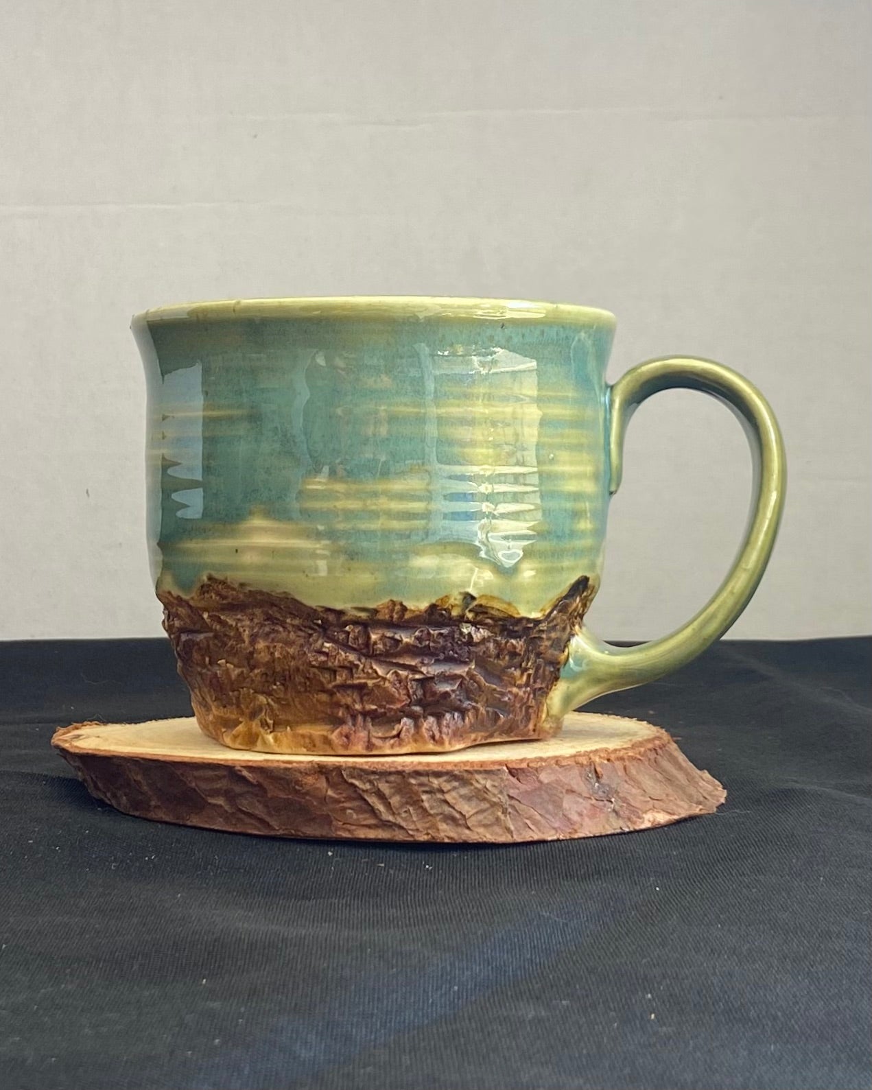 Handcrafted Mountain Mug with glossy celadon sky glaze and rocky textured mountainscape, accented with iron oxide and matte amber quartz glaze. Unique ceramic mug inspired by outdoor rock climbing, perfect for coffee or tea. Artisan quality, wabi sabi design, and playful glaze details