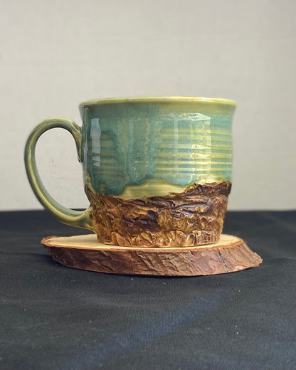 Handcrafted Mountain Mug with glossy celadon sky glaze and rocky textured mountainscape, accented with iron oxide and matte amber quartz glaze. Unique ceramic mug inspired by outdoor rock climbing, perfect for coffee or tea. Artisan quality, wabi sabi design, and playful glaze details