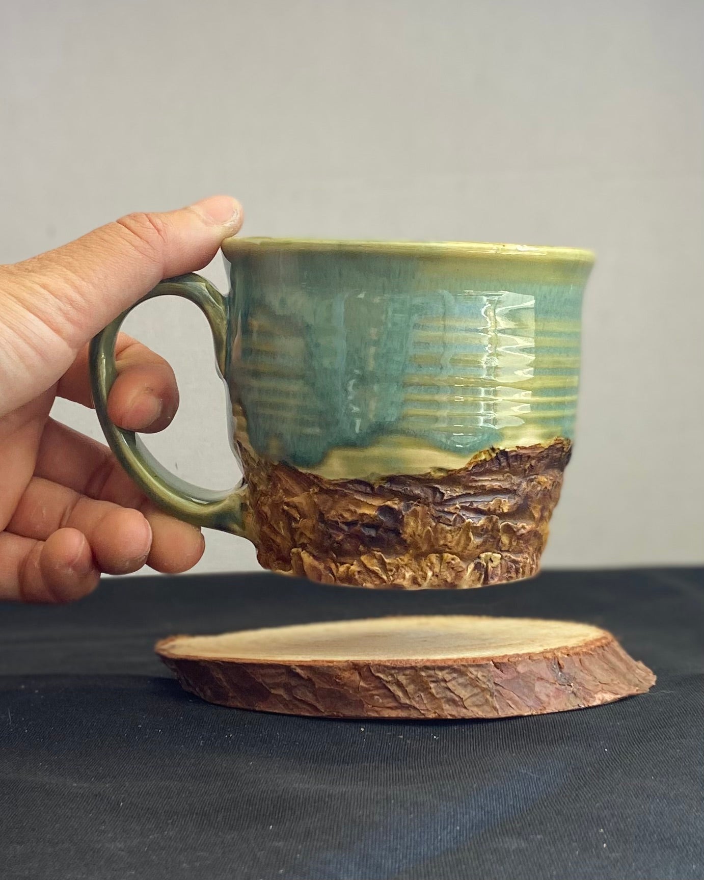 Handcrafted Mountain Mug with glossy celadon sky glaze and rocky textured mountainscape, accented with iron oxide and matte amber quartz glaze. Unique ceramic mug inspired by outdoor rock climbing, perfect for coffee or tea. Artisan quality, wabi sabi design, and playful glaze details