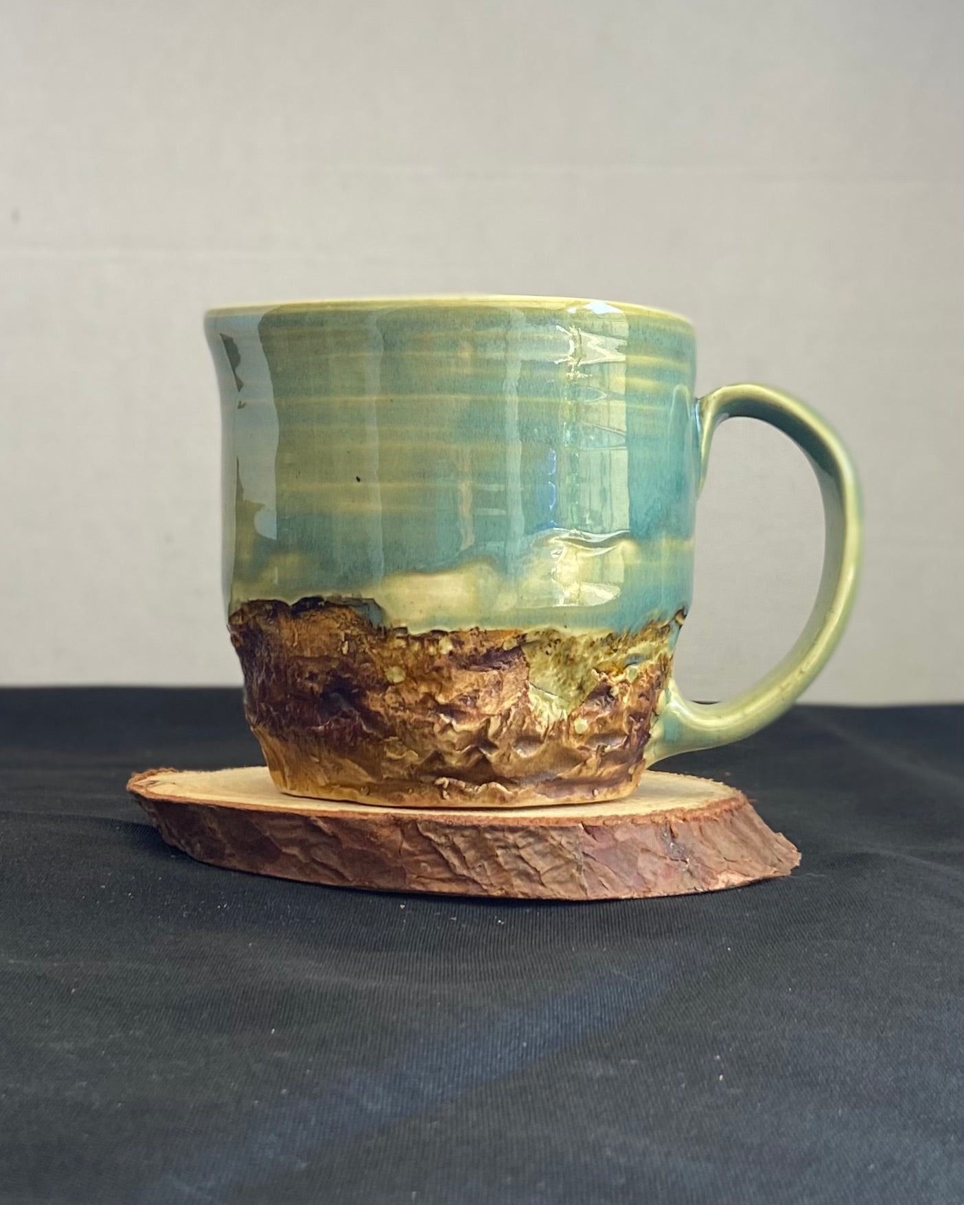 Handcrafted Mountain Mug with glossy celadon sky glaze and rocky textured mountainscape, accented with iron oxide and matte amber quartz glaze. Unique ceramic mug inspired by outdoor rock climbing, perfect for coffee or tea. Artisan quality, wabi sabi design, and playful glaze details