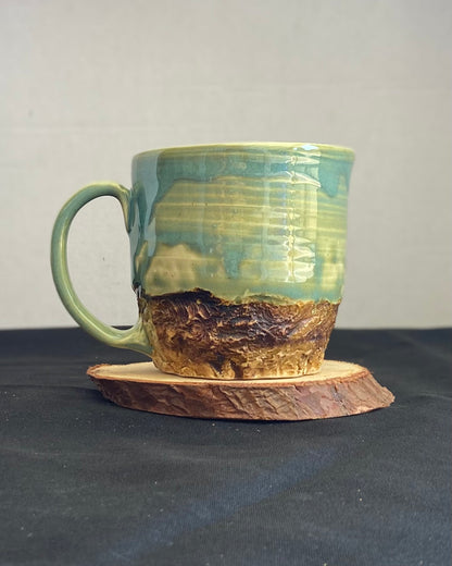 Handcrafted Mountain Mug with glossy celadon sky glaze and rocky textured mountainscape, accented with iron oxide and matte amber quartz glaze. Unique ceramic mug inspired by outdoor rock climbing, perfect for coffee or tea. Artisan quality, wabi sabi design, and playful glaze details