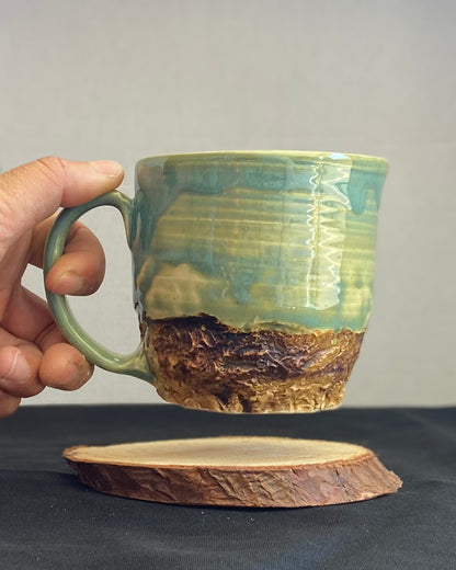 Handcrafted Mountain Mug with glossy celadon sky glaze and rocky textured mountainscape, accented with iron oxide and matte amber quartz glaze. Unique ceramic mug inspired by outdoor rock climbing, perfect for coffee or tea. Artisan quality, wabi sabi design, and playful glaze details