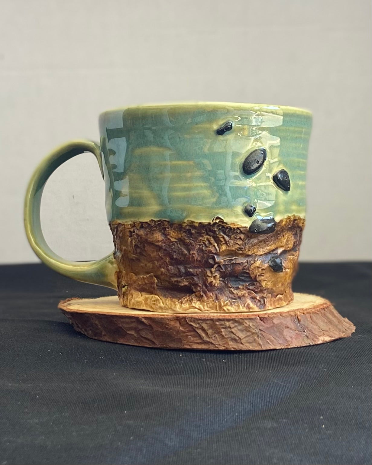 Handcrafted Boulder Mug with glossy celadon sky glaze and rocky textured mountainscape, featuring miniature black rock climbing holds with tiny bolt holes. Unique ceramic mug inspired by indoor and outdoor rock climbing adventures, perfect for climbers. Artisan quality, wabi sabi design, and playful glaze details.