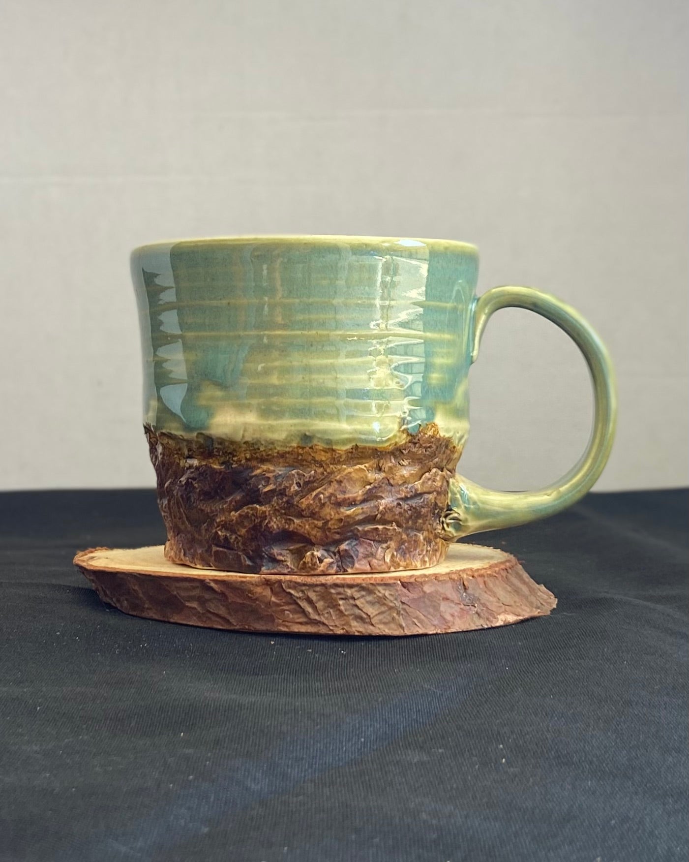 Handcrafted Boulder Mug with glossy celadon sky glaze and rocky textured mountainscape, featuring miniature black rock climbing holds with tiny bolt holes. Unique ceramic mug inspired by indoor and outdoor rock climbing adventures, perfect for climbers. Artisan quality, wabi sabi design, and playful glaze details.