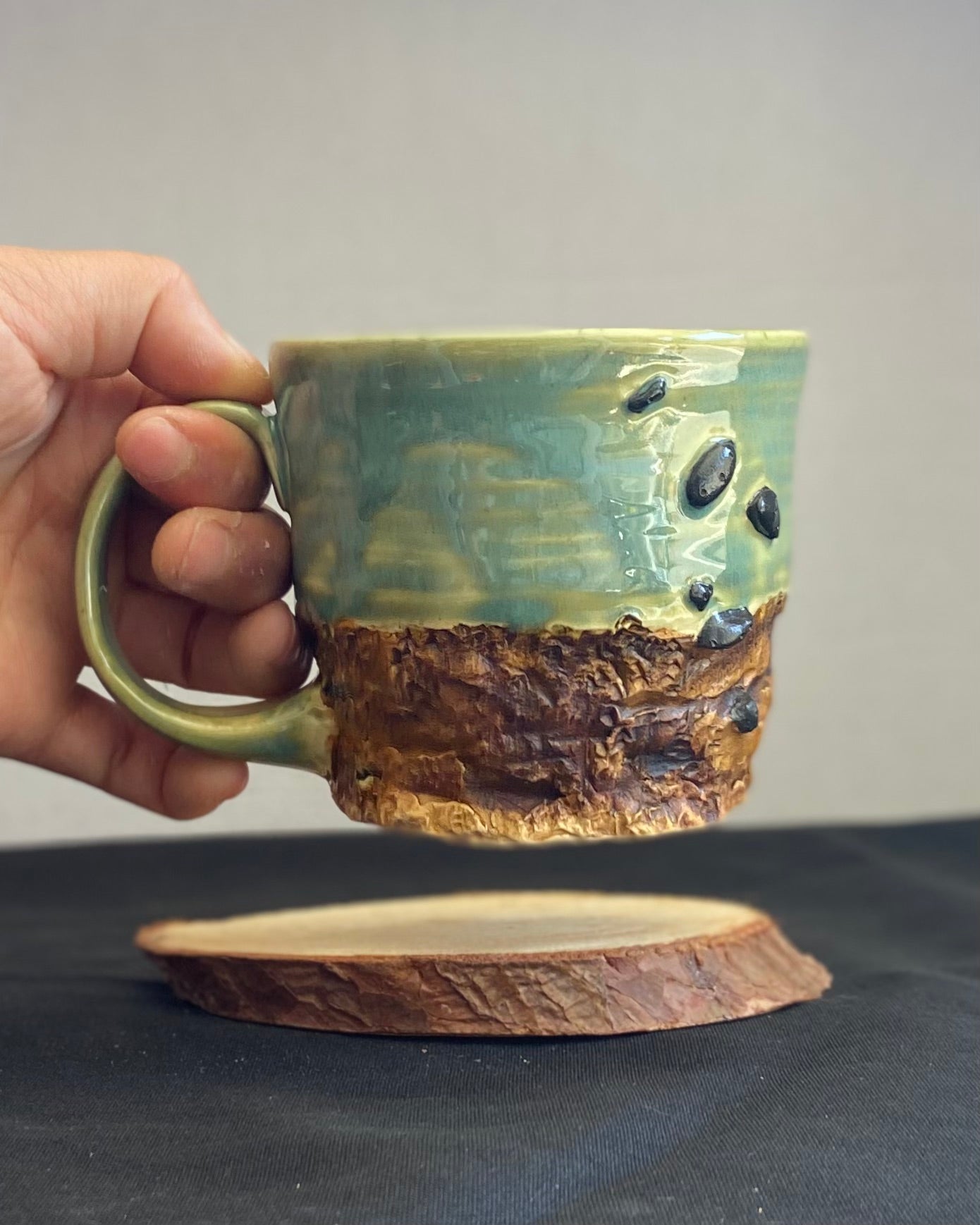 Handcrafted Boulder Mug with glossy celadon sky glaze and rocky textured mountainscape, featuring miniature black rock climbing holds with tiny bolt holes. Unique ceramic mug inspired by indoor and outdoor rock climbing adventures, perfect for climbers. Artisan quality, wabi sabi design, and playful glaze details.