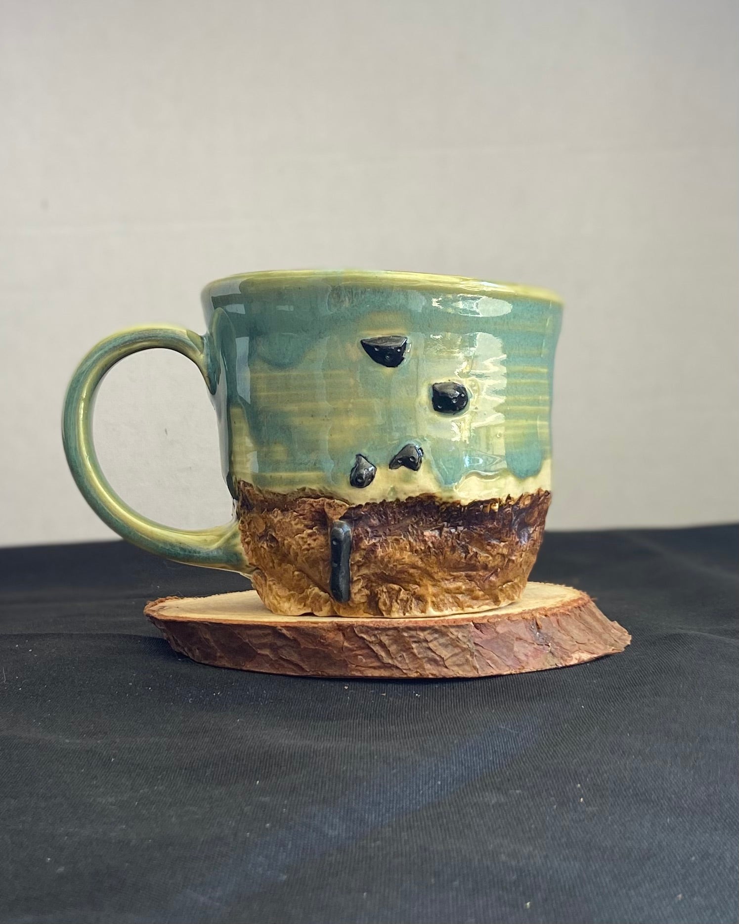 Handcrafted Boulder Mug with glossy celadon sky glaze and rocky textured mountainscape, featuring miniature black rock climbing holds with tiny bolt holes. Unique ceramic mug inspired by indoor and outdoor rock climbing adventures, perfect for climbers. Artisan quality, wabi sabi design, and playful glaze details.