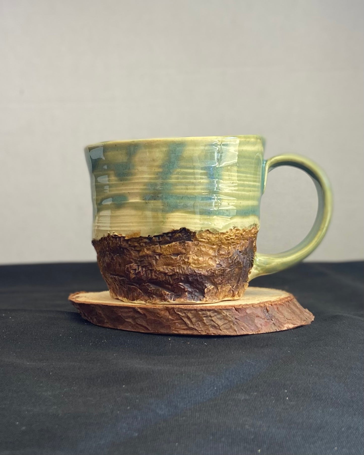 Handcrafted Boulder Mug with glossy celadon sky glaze and rocky textured mountainscape, featuring miniature black rock climbing holds with tiny bolt holes. Unique ceramic mug inspired by indoor and outdoor rock climbing adventures, perfect for climbers. Artisan quality, wabi sabi design, and playful glaze details.