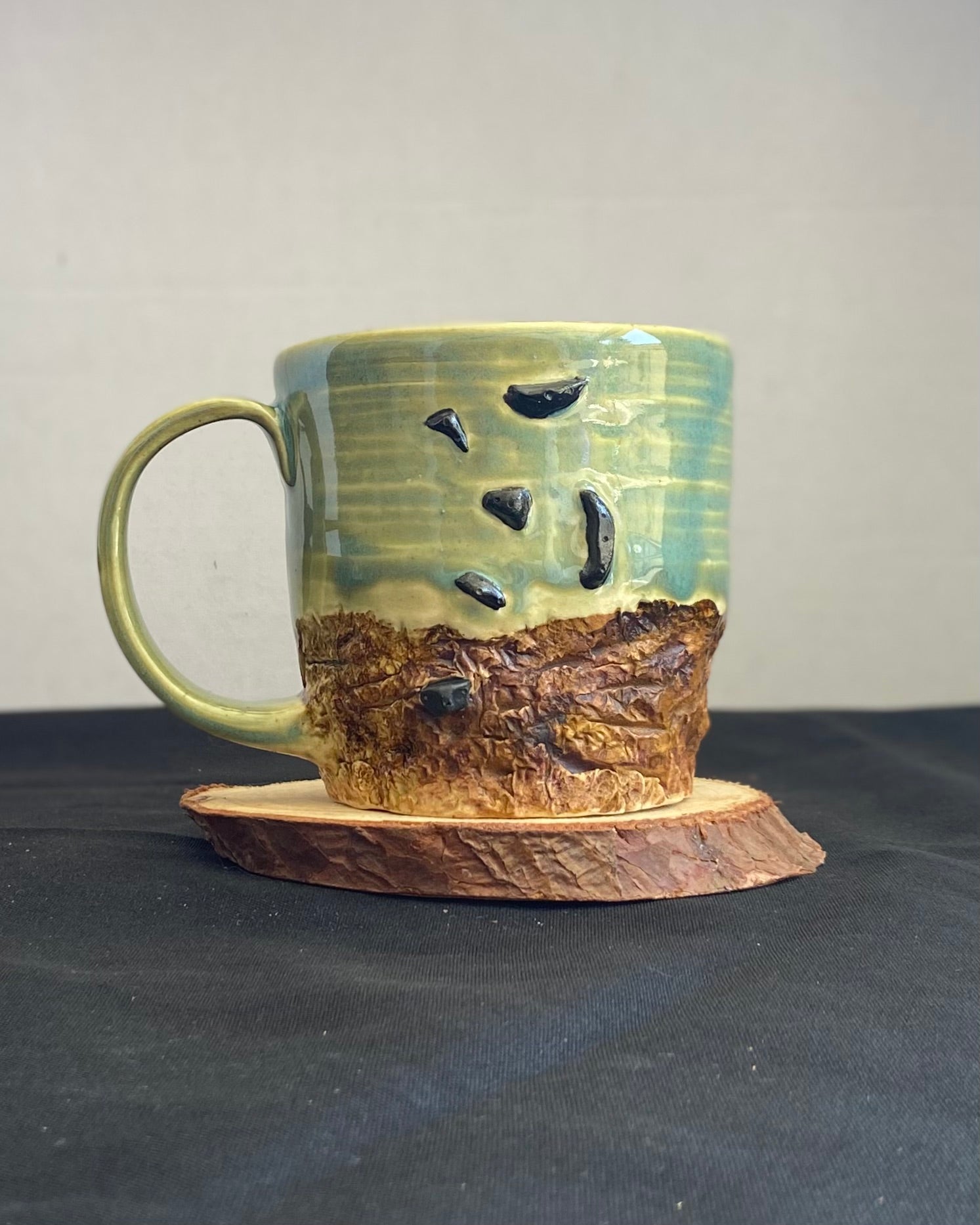 Handcrafted Boulder Mug with glossy celadon sky glaze and rocky textured mountainscape, featuring miniature black rock climbing holds with tiny bolt holes. Unique ceramic mug inspired by indoor and outdoor rock climbing adventures, perfect for climbers. Artisan quality, wabi sabi design, and playful glaze details.