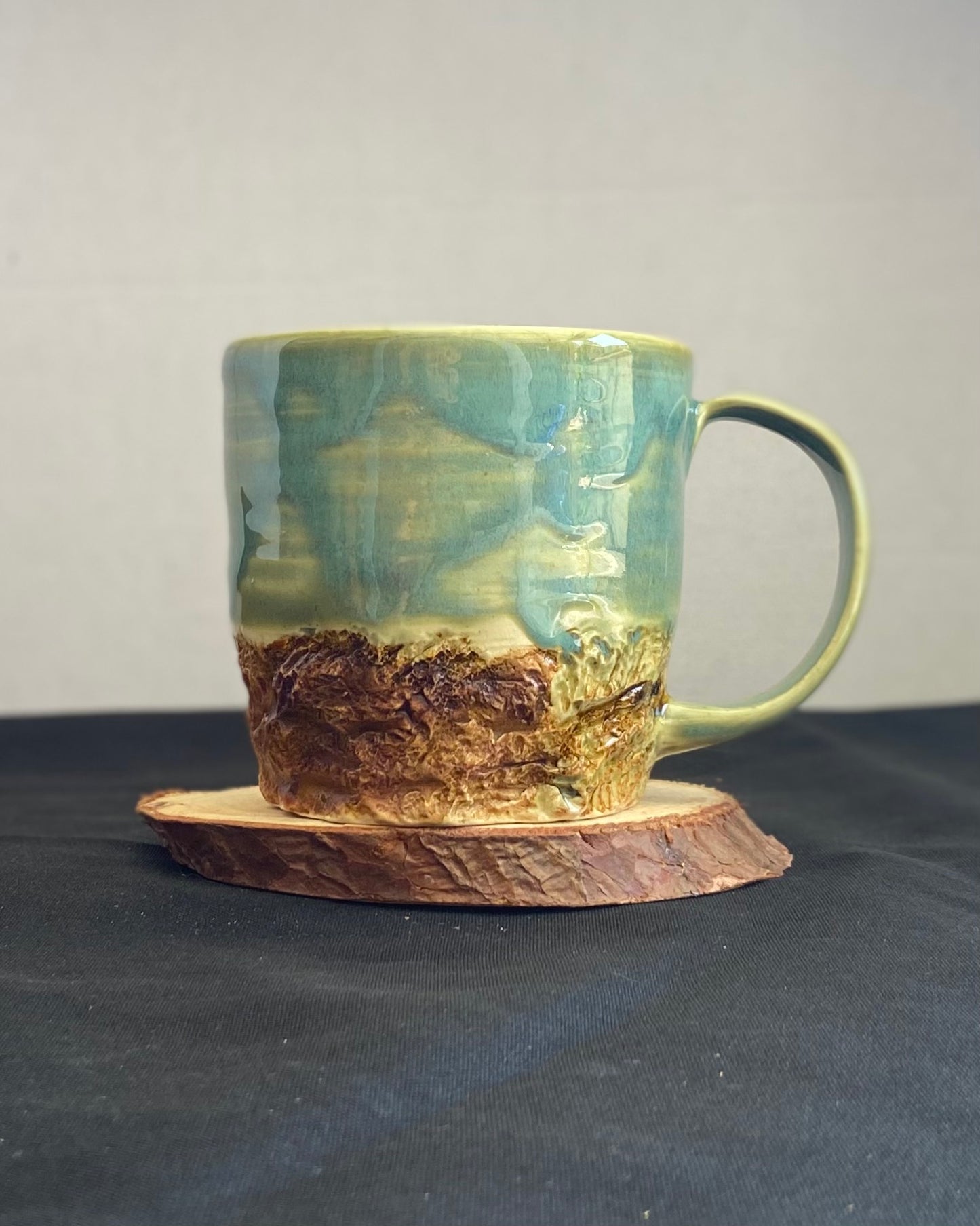 Handcrafted Boulder Mug with glossy celadon sky glaze and rocky textured mountainscape, featuring miniature black rock climbing holds with tiny bolt holes. Unique ceramic mug inspired by indoor and outdoor rock climbing adventures, perfect for climbers. Artisan quality, wabi sabi design, and playful glaze details.