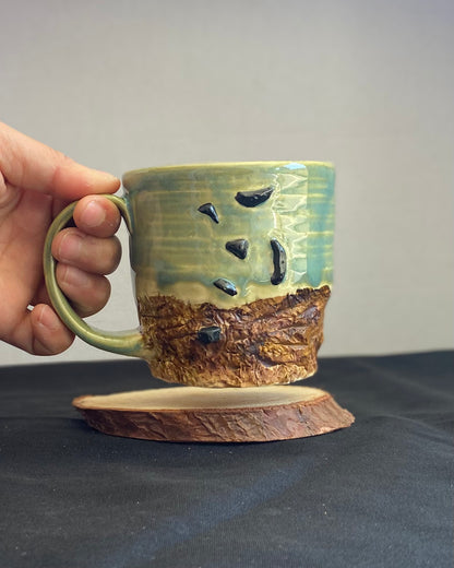 Handcrafted Boulder Mug with glossy celadon sky glaze and rocky textured mountainscape, featuring miniature black rock climbing holds with tiny bolt holes. Unique ceramic mug inspired by indoor and outdoor rock climbing adventures, perfect for climbers. Artisan quality, wabi sabi design, and playful glaze details.