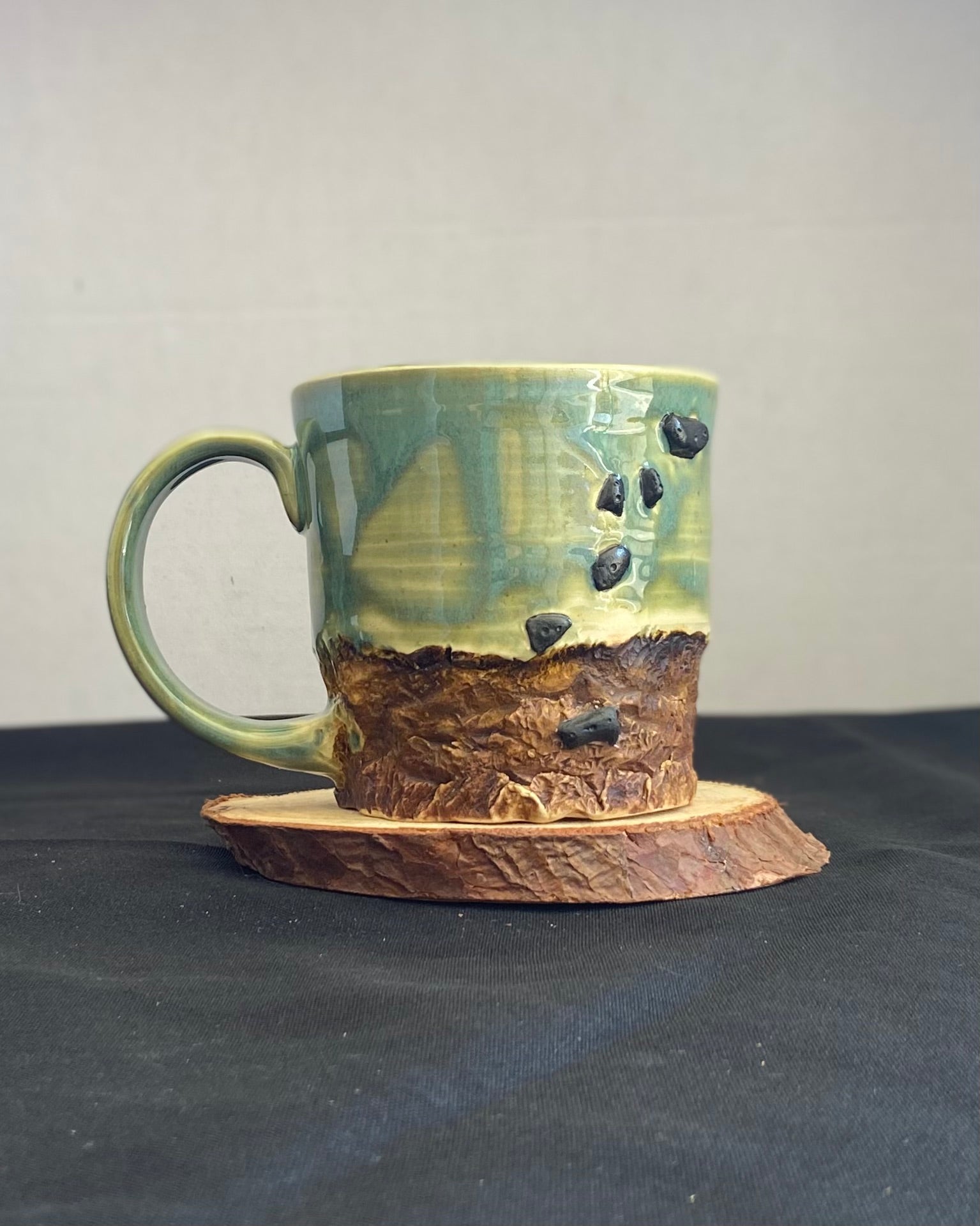 Handcrafted Boulder Mug with glossy celadon sky glaze and rocky textured mountainscape, featuring miniature black rock climbing holds with tiny bolt holes. Unique ceramic mug inspired by indoor and outdoor rock climbing adventures, perfect for climbers. Artisan quality, wabi sabi design, and playful glaze details.