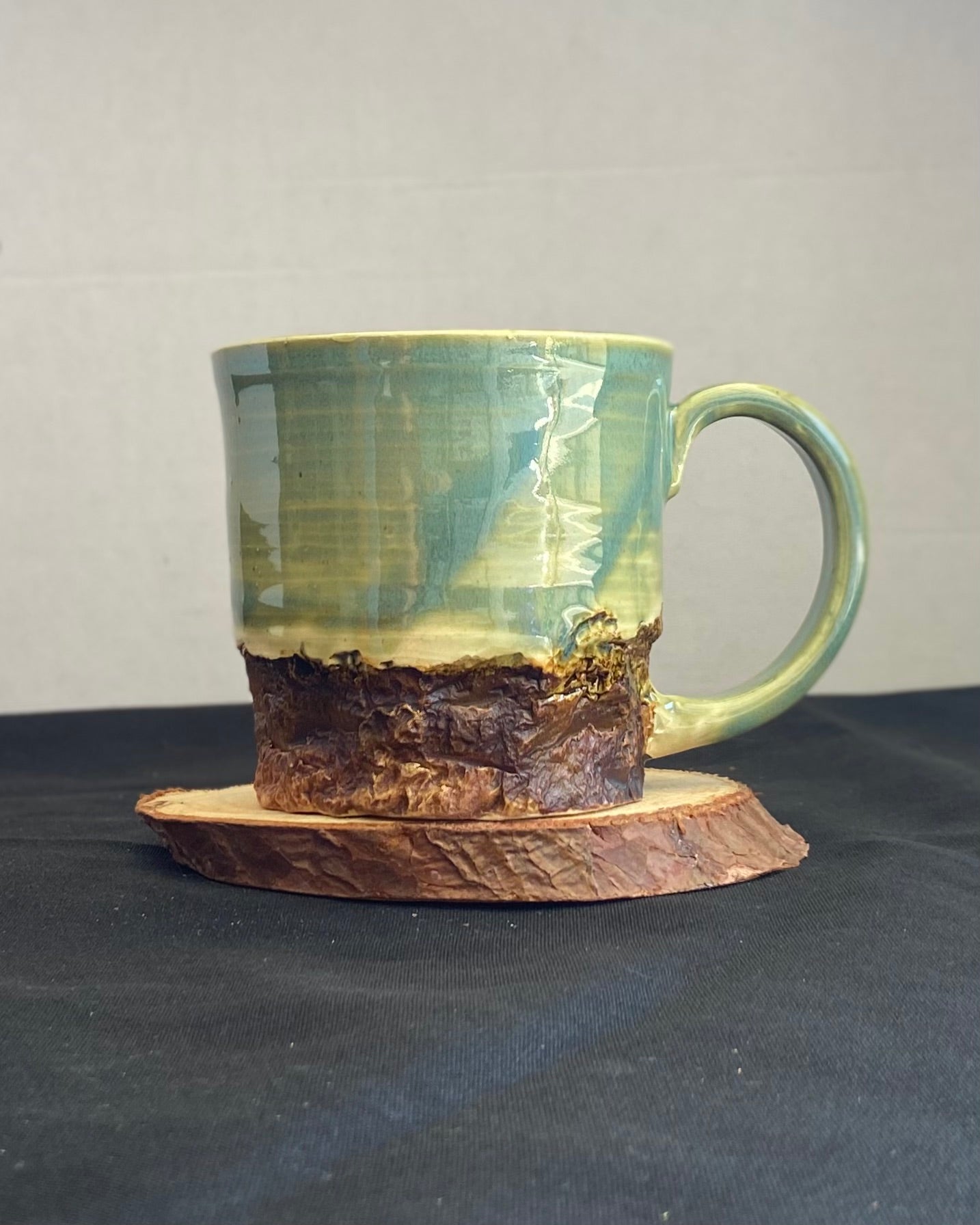 Handcrafted Boulder Mug with glossy celadon sky glaze and rocky textured mountainscape, featuring miniature black rock climbing holds with tiny bolt holes. Unique ceramic mug inspired by indoor and outdoor rock climbing adventures, perfect for climbers. Artisan quality, wabi sabi design, and playful glaze details.