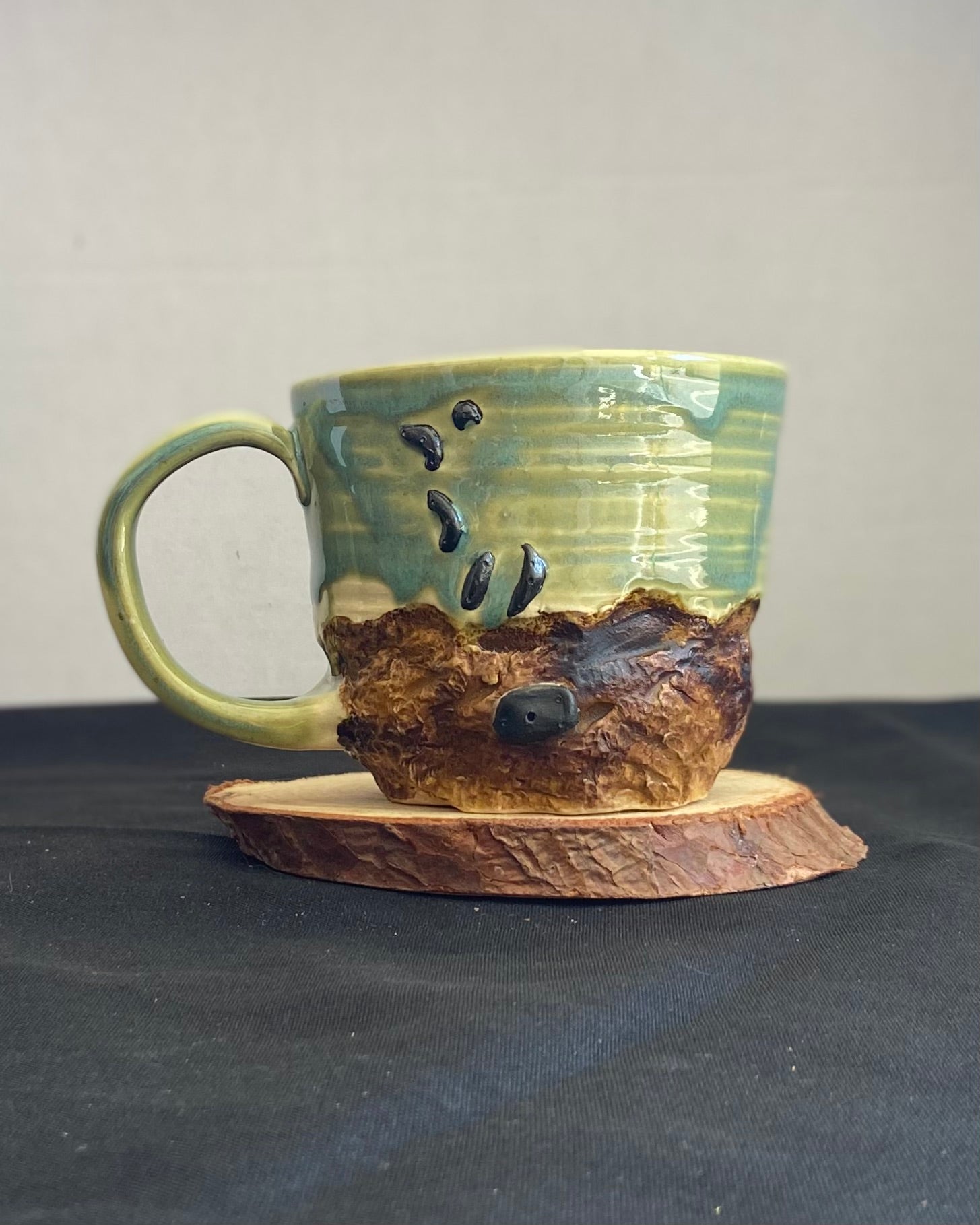 Handcrafted Boulder Mug with glossy celadon sky glaze and rocky textured mountainscape, featuring miniature black rock climbing holds with tiny bolt holes. Unique ceramic mug inspired by indoor and outdoor rock climbing adventures, perfect for climbers. Artisan quality, wabi sabi design, and playful glaze details.