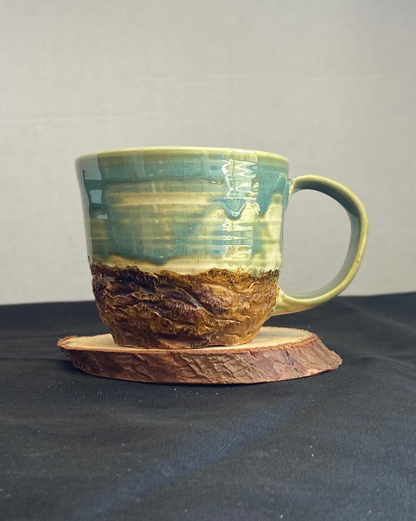 Handcrafted Boulder Mug with glossy celadon sky glaze and rocky textured mountainscape, featuring miniature black rock climbing holds with tiny bolt holes. Unique ceramic mug inspired by indoor and outdoor rock climbing adventures, perfect for climbers. Artisan quality, wabi sabi design, and playful glaze details.