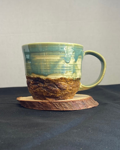 Handcrafted Boulder Mug with glossy celadon sky glaze and rocky textured mountainscape, featuring miniature black rock climbing holds with tiny bolt holes. Unique ceramic mug inspired by indoor and outdoor rock climbing adventures, perfect for climbers. Artisan quality, wabi sabi design, and playful glaze details.