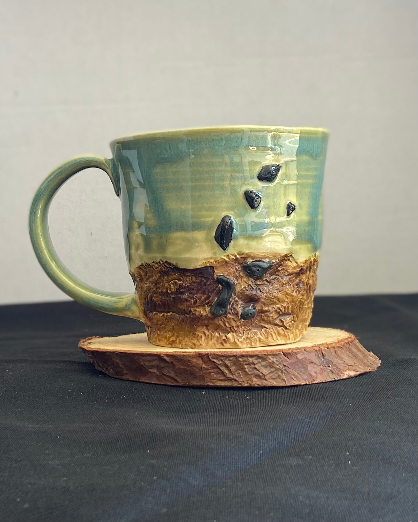 Handcrafted Boulder Mug with glossy celadon sky glaze and rocky textured mountainscape, featuring miniature black rock climbing holds with tiny bolt holes. Unique ceramic mug inspired by indoor and outdoor rock climbing adventures, perfect for climbers. Artisan quality, wabi sabi design, and playful glaze details.