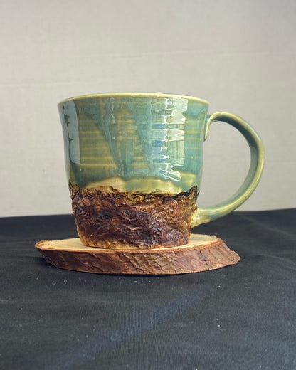 Handcrafted Boulder Mug with glossy celadon sky glaze and rocky textured mountainscape, featuring miniature black rock climbing holds with tiny bolt holes. Unique ceramic mug inspired by indoor and outdoor rock climbing adventures, perfect for climbers. Artisan quality, wabi sabi design, and playful glaze details.