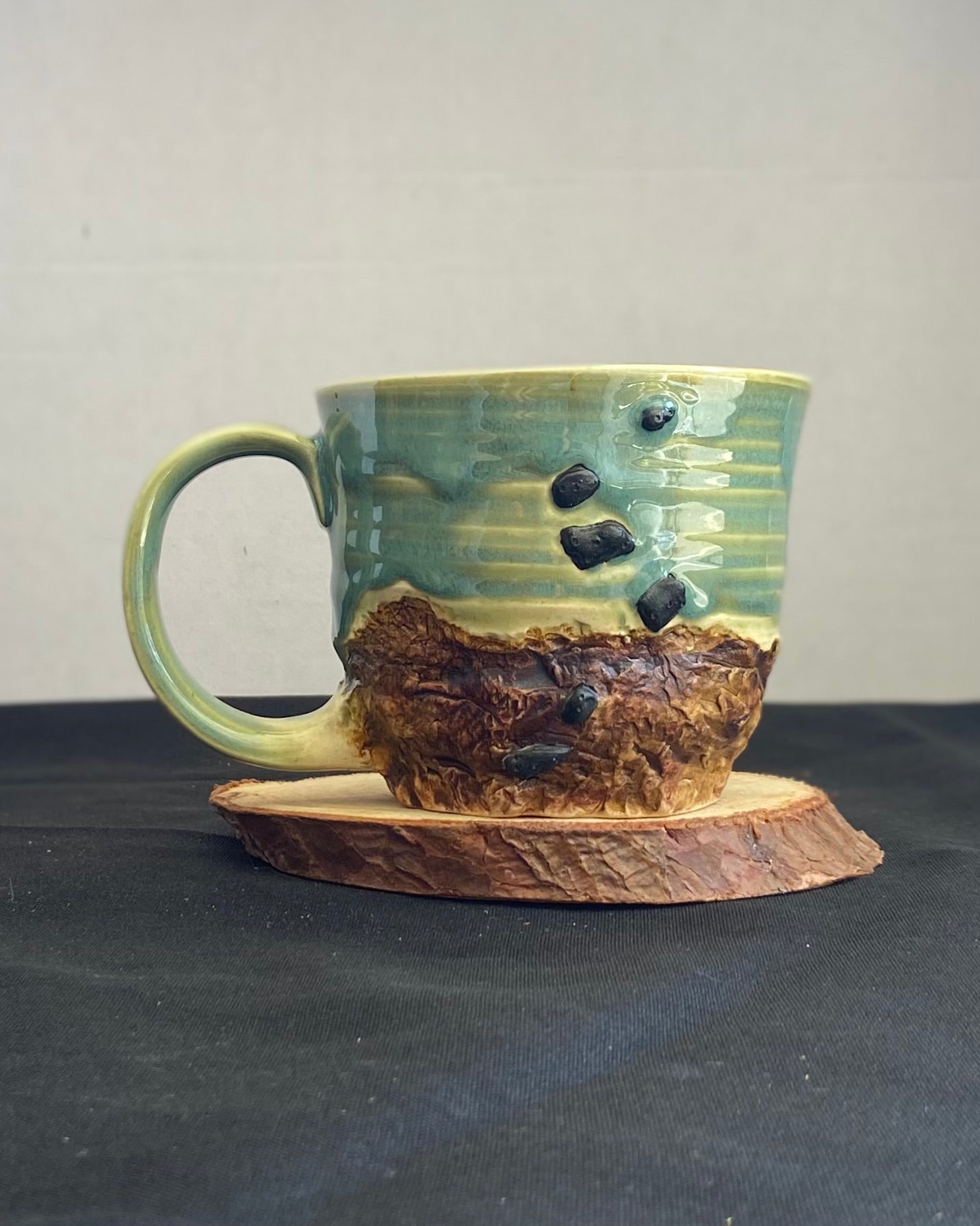 Handcrafted Boulder Mug with glossy celadon sky glaze and rocky textured mountainscape, featuring miniature black rock climbing holds with tiny bolt holes. Unique ceramic mug inspired by indoor and outdoor rock climbing adventures, perfect for climbers. Artisan quality, wabi sabi design, and playful glaze details.