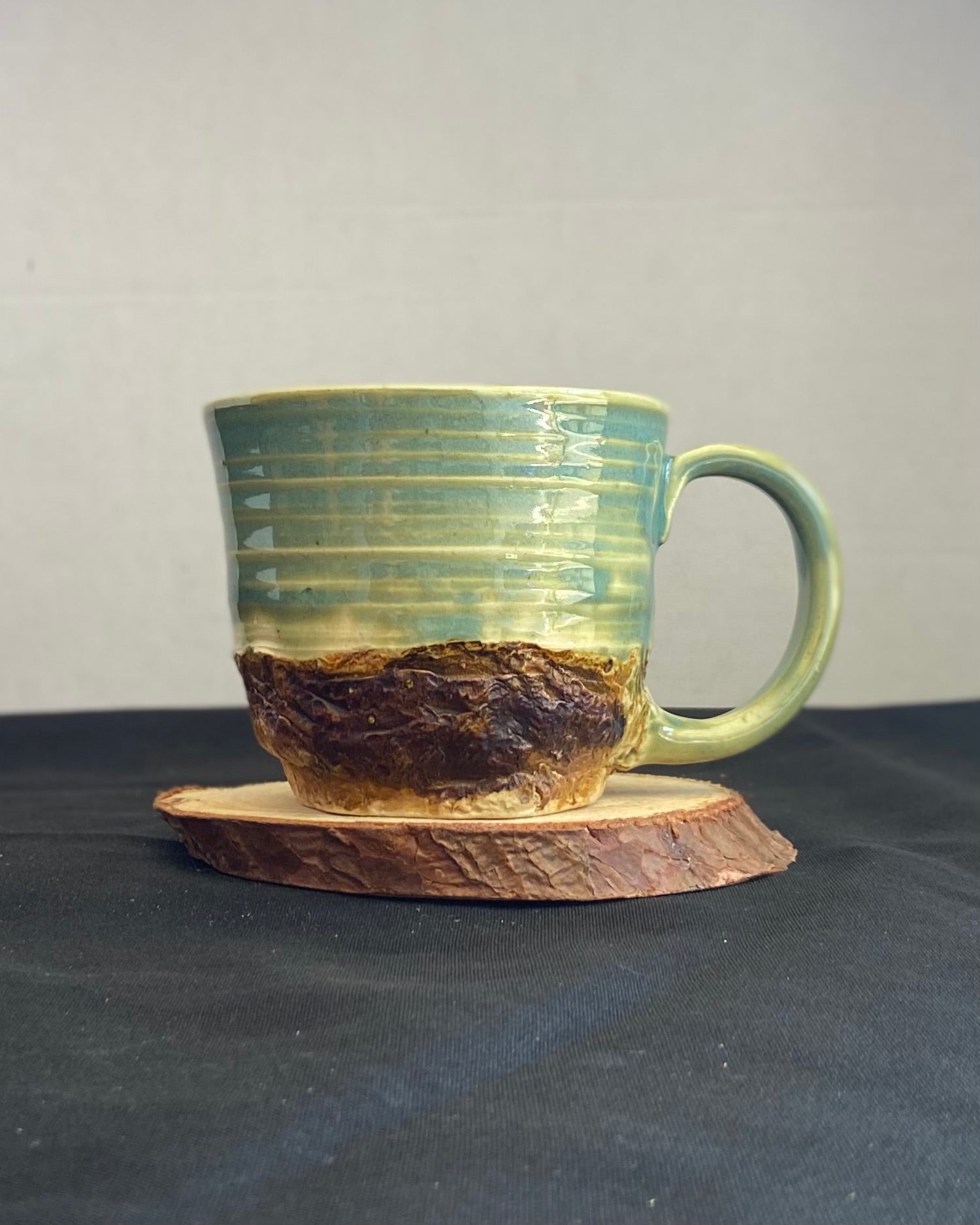 Handcrafted Boulder Mug with glossy celadon sky glaze and rocky textured mountainscape, featuring miniature black rock climbing holds with tiny bolt holes. Unique ceramic mug inspired by indoor and outdoor rock climbing adventures, perfect for climbers. Artisan quality, wabi sabi design, and playful glaze details.