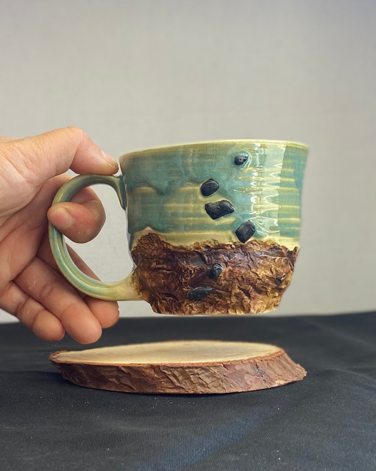 Handcrafted Boulder Mug with glossy celadon sky glaze and rocky textured mountainscape, featuring miniature black rock climbing holds with tiny bolt holes. Unique ceramic mug inspired by indoor and outdoor rock climbing adventures, perfect for climbers. Artisan quality, wabi sabi design, and playful glaze details.