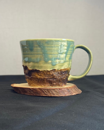 Handcrafted Boulder Mug with glossy celadon sky glaze and rocky textured mountainscape, featuring miniature black rock climbing holds with tiny bolt holes. Unique ceramic mug inspired by indoor and outdoor rock climbing adventures, perfect for climbers. Artisan quality, wabi sabi design, and playful glaze details.