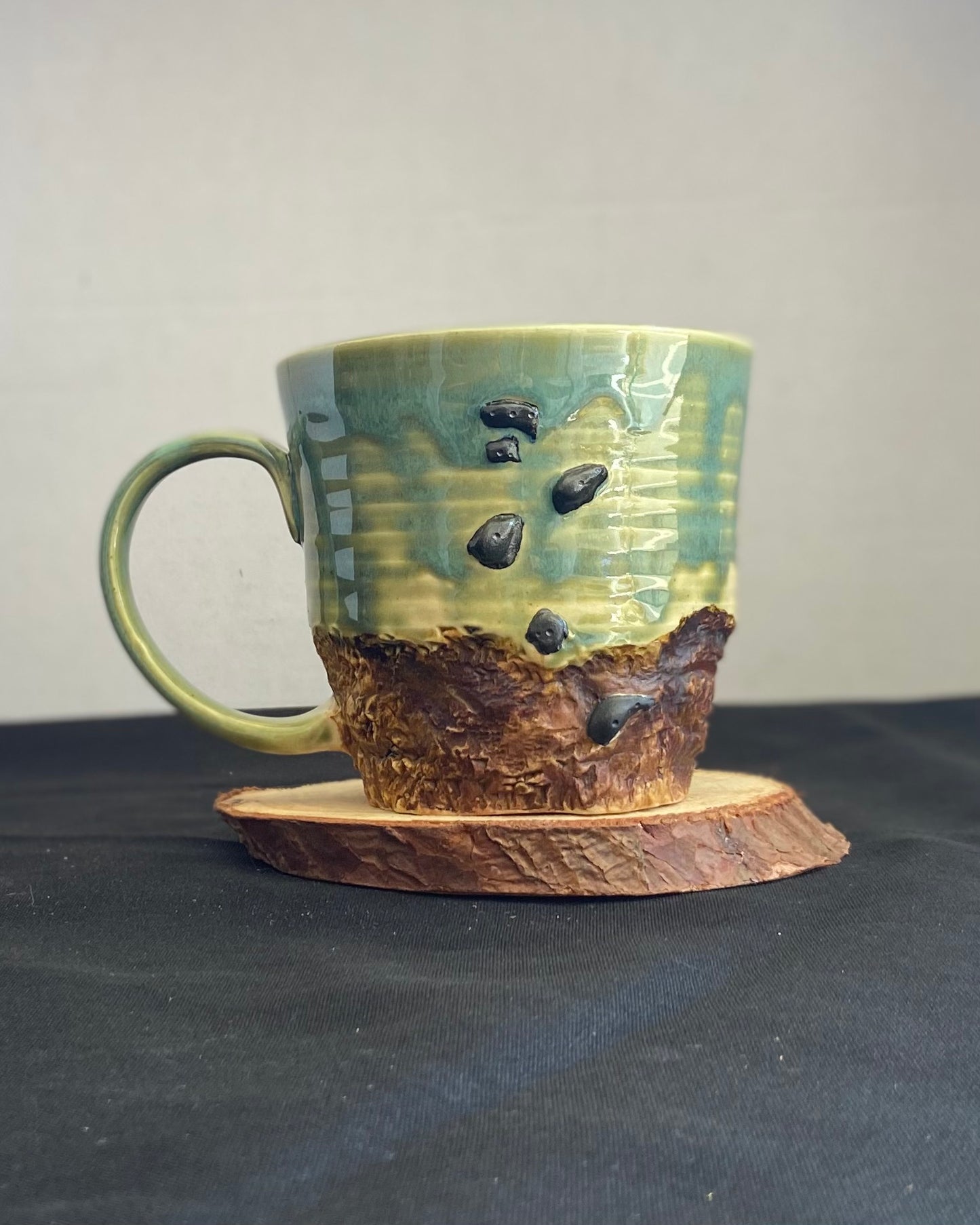 Handcrafted Boulder Mug with glossy celadon sky glaze and rocky textured mountainscape, featuring miniature black rock climbing holds with tiny bolt holes. Unique ceramic mug inspired by indoor and outdoor rock climbing adventures, perfect for climbers. Artisan quality, wabi sabi design, and playful glaze details. Hand-etched joshua tree.