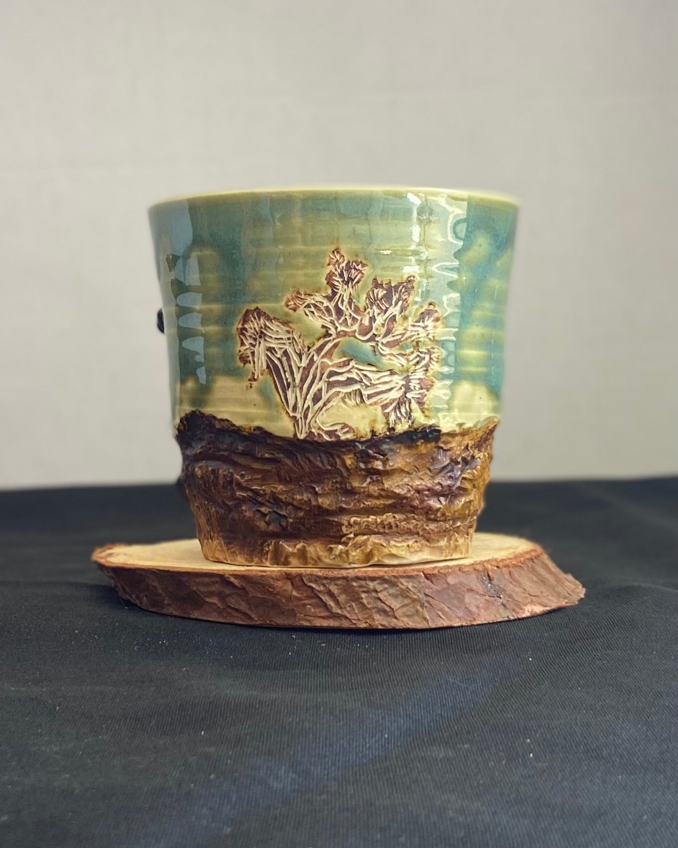 Handcrafted Boulder Mug with glossy celadon sky glaze and rocky textured mountainscape, featuring miniature black rock climbing holds with tiny bolt holes. Unique ceramic mug inspired by indoor and outdoor rock climbing adventures, perfect for climbers. Artisan quality, wabi sabi design, and playful glaze details. Hand-etched joshua tree.