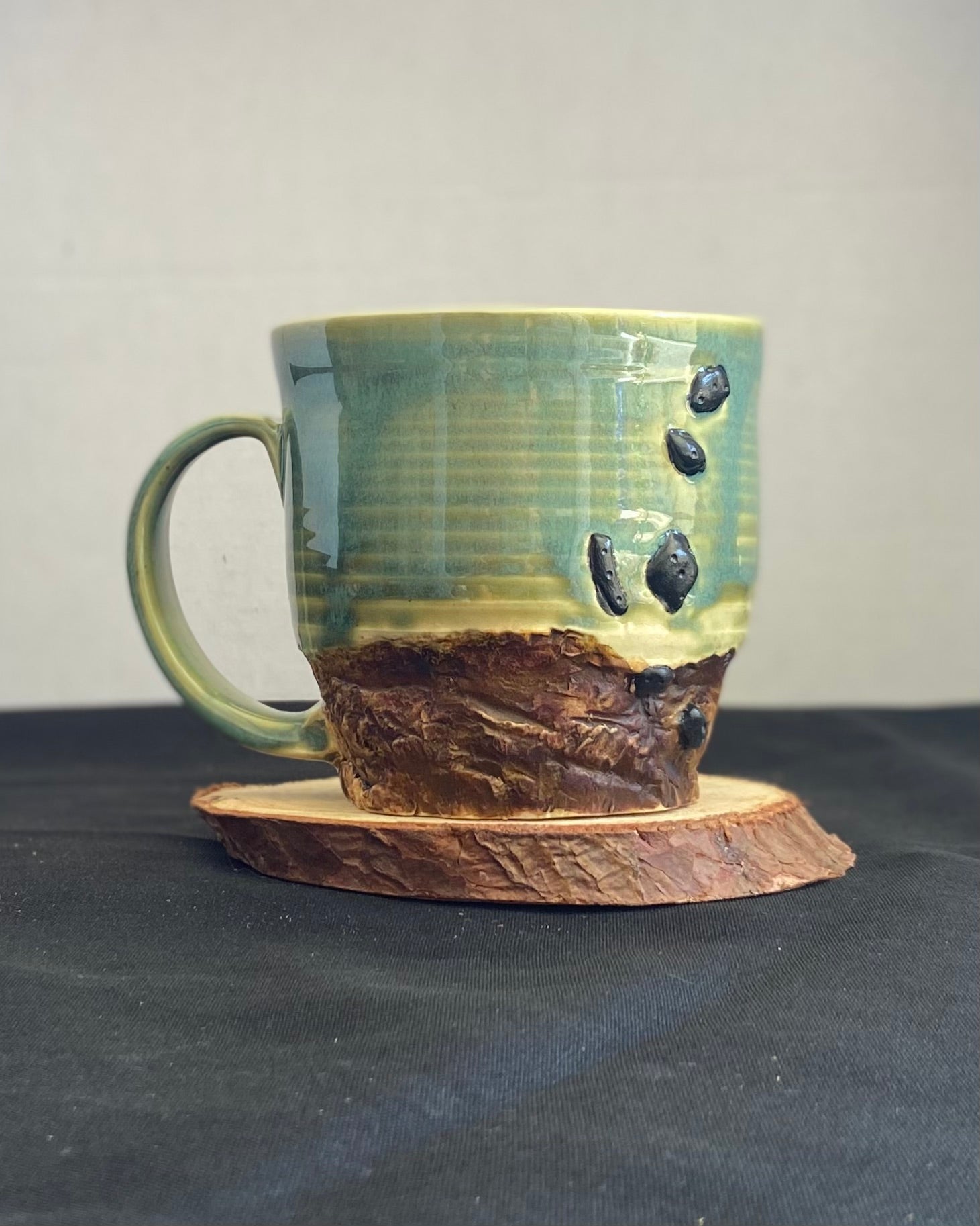 Handcrafted Boulder Mug with glossy celadon sky glaze and rocky textured mountainscape, featuring miniature black rock climbing holds with tiny bolt holes. Unique ceramic mug inspired by indoor and outdoor rock climbing adventures, perfect for climbers. Artisan quality, wabi sabi design, and playful glaze details. Hand-etched joshua tree.