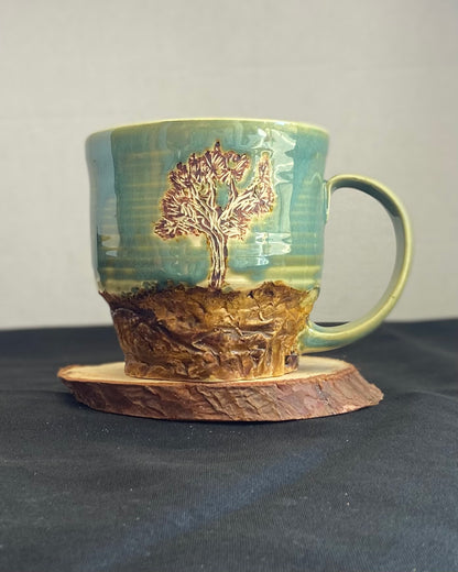 Handcrafted Boulder Mug with glossy celadon sky glaze and rocky textured mountainscape, featuring miniature black rock climbing holds with tiny bolt holes. Unique ceramic mug inspired by indoor and outdoor rock climbing adventures, perfect for climbers. Artisan quality, wabi sabi design, and playful glaze details. Hand-etched joshua tree.