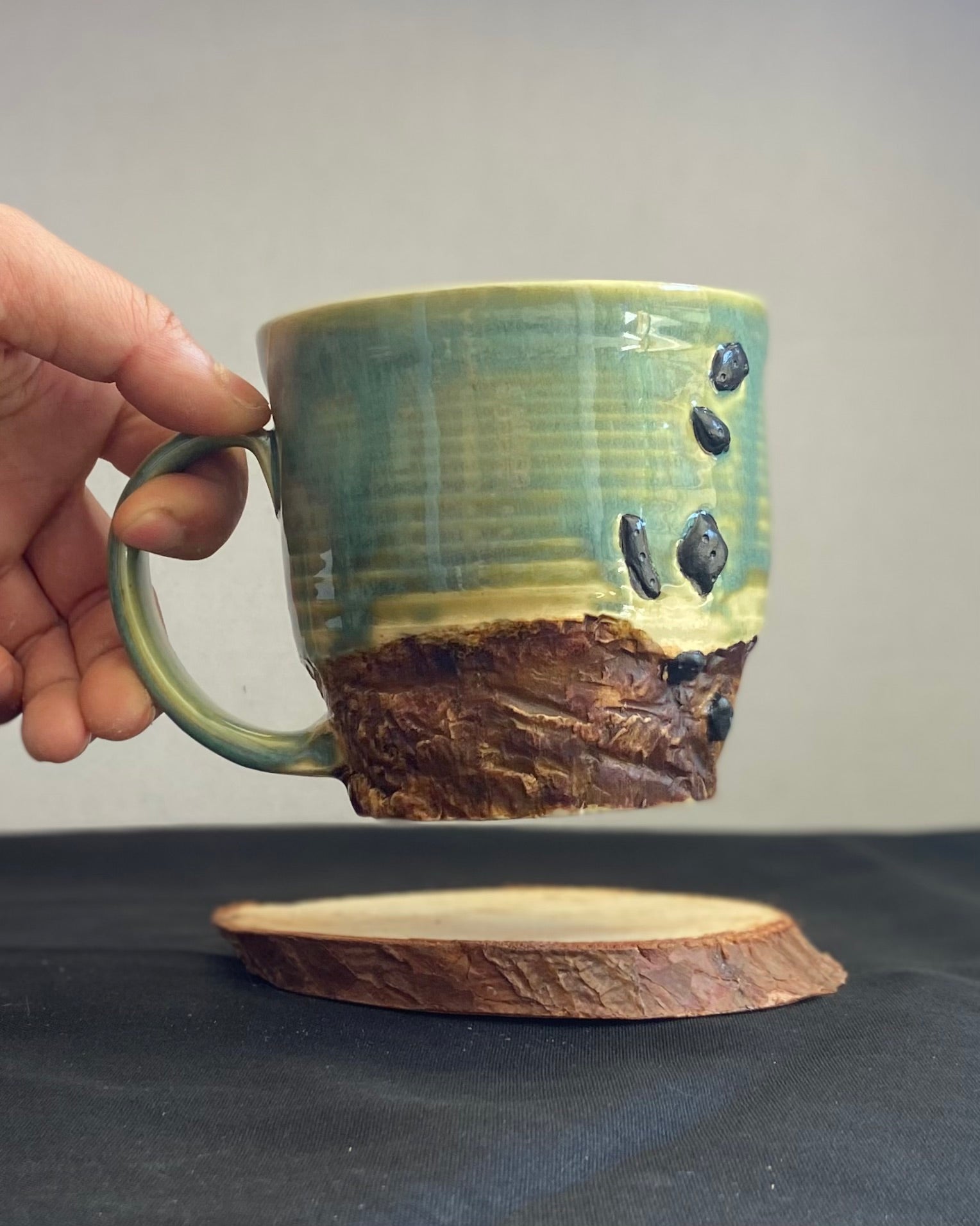 Handcrafted Boulder Mug with glossy celadon sky glaze and rocky textured mountainscape, featuring miniature black rock climbing holds with tiny bolt holes. Unique ceramic mug inspired by indoor and outdoor rock climbing adventures, perfect for climbers. Artisan quality, wabi sabi design, and playful glaze details. Hand-etched joshua tree.