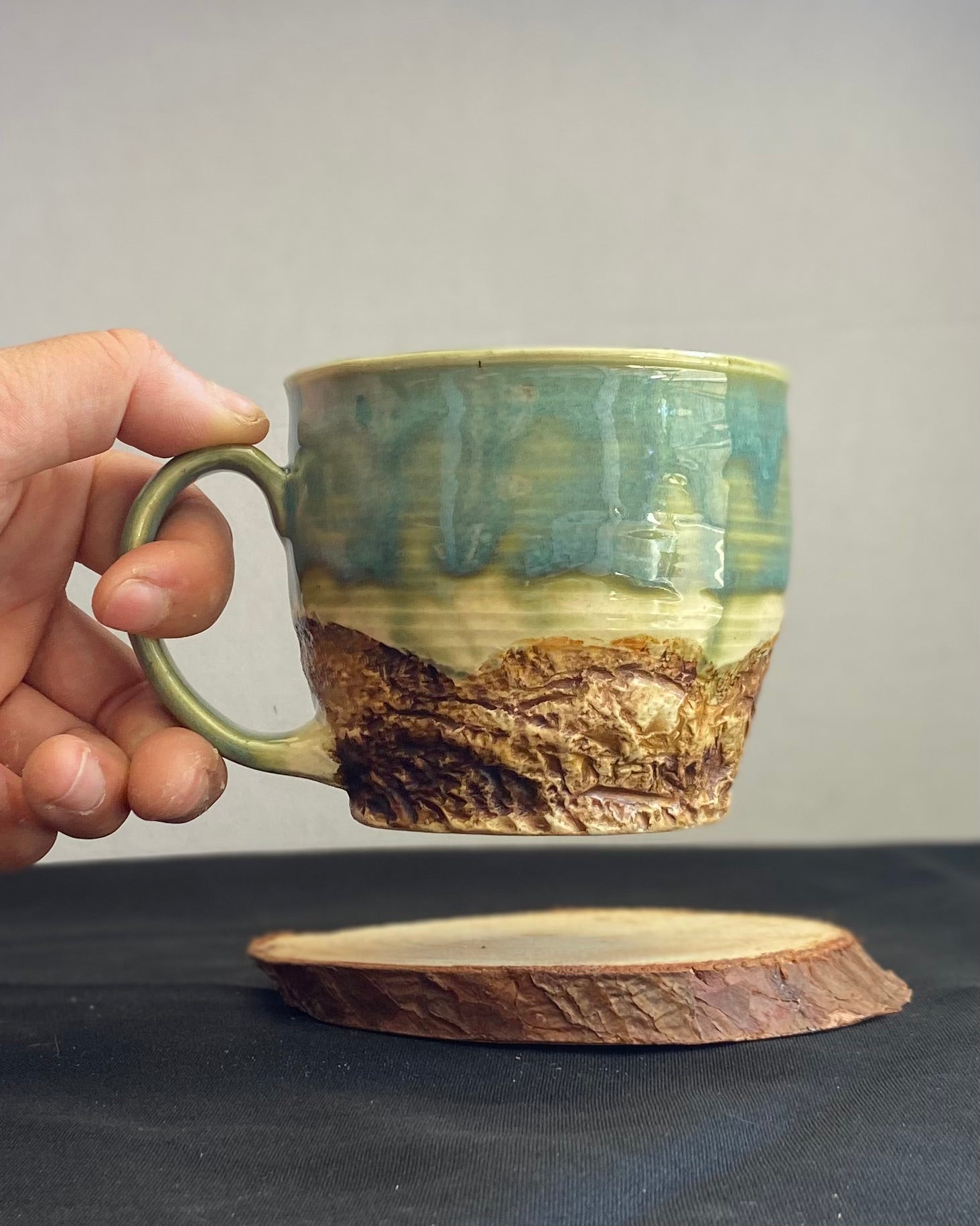 Handcrafted Mountain Mug with glossy celadon sky glaze and rocky textured mountainscape, accented with iron oxide and matte amber quartz glaze. Unique ceramic mug inspired by outdoor rock climbing, perfect for coffee or tea. Artisan quality, wabi sabi design, and playful glaze details