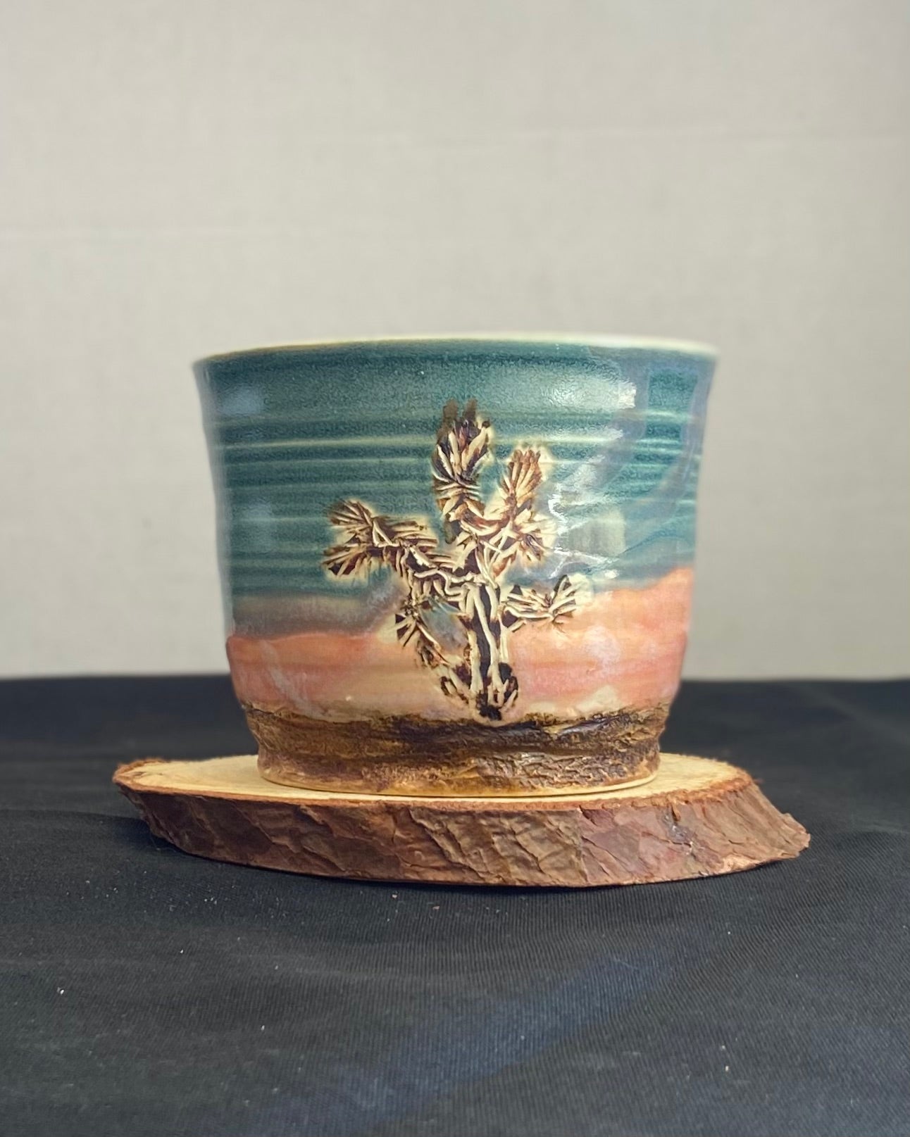 Handcrafted tumbler with hand-etched Joshua tree, antique blue satin glaze, and sunburnt pink glaze creating a sunset over a hand-carved mountain landscape. Unique ceramic tumbler inspired by nature, perfect for beverages. Artisan quality, wabi sabi design, and nature-inspired aesthetic