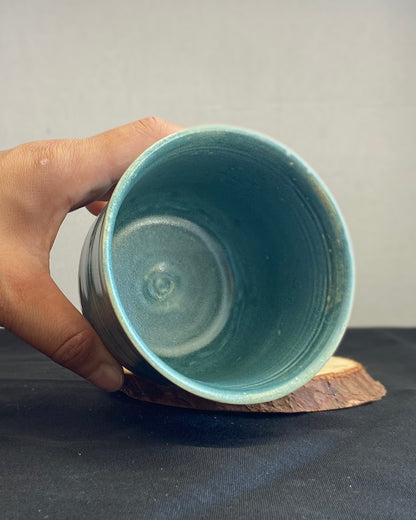 Handcrafted tumbler with hand-etched Joshua tree, antique blue satin glaze, and sunburnt pink glaze creating a sunset over a hand-carved mountain landscape. Unique ceramic tumbler inspired by nature, perfect for beverages. Artisan quality, wabi sabi design, and nature-inspired aesthetic