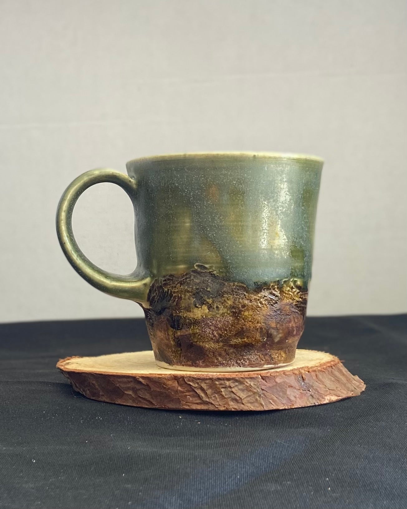 Handthrown ceramic mug, sage matte glazed with amber-iron oxide wash. Dual-texture surface, matte. Rock-hammered rugged mountain landscape, hand-pulled handle. Fired to cone 5.