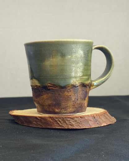 Handthrown ceramic mug, sage matte glazed with amber-iron oxide wash. Dual-texture surface, matte. Rock-hammered rugged mountain landscape, hand-pulled handle. Fired to cone 5.