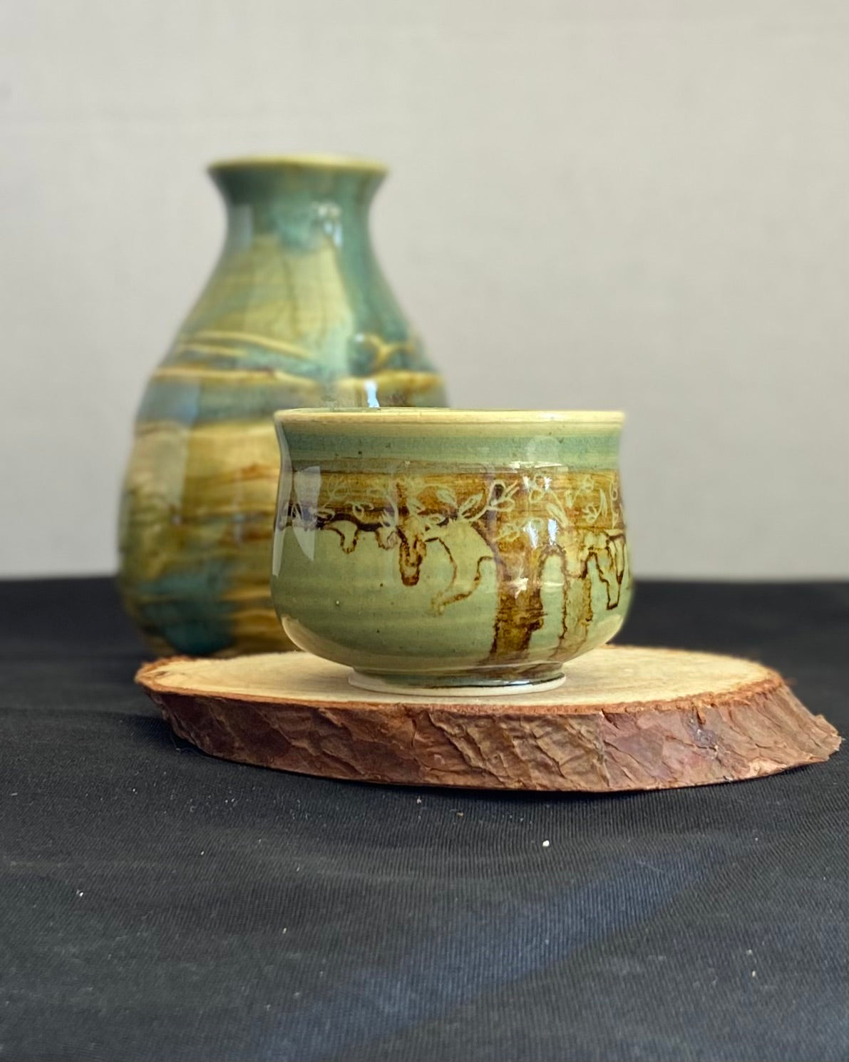 Handcrafted sake set with one pourer and two cups, featuring celadon glaze over textured carvings to evoke water. Cups have dripping iron oxide accents and tulips carved on the lip. Unique ceramic sake set inspired by nature, perfect for serving sake. Artisan quality, wabi sabi design, and nature-inspired aesthetic